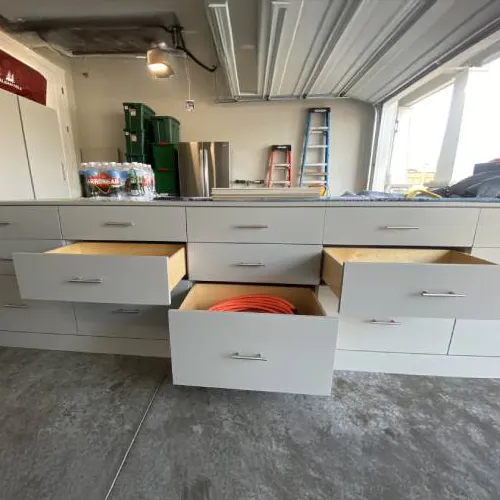 Heavy-duty garage storage solution by PNW Closets featuring a long bank of light grey drawers with sturdy metal handles, shown partially open to reveal spacious interior storage.