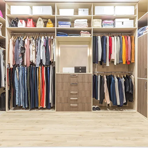 PNW Closets custom walk-in organization system featuring a mix of light wood shelving, double-hang clothing rods, and a central dresser unit with five drawers for maximum storage.