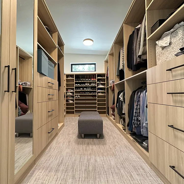 Custom walk-in closet with light wood shelving, shoe storage, and center dressing bench